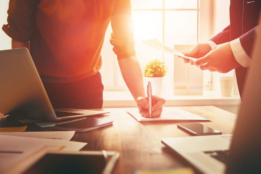 Two people working together at a desk, reviewing documents and writing notes, representing the process of creating a will or trust.