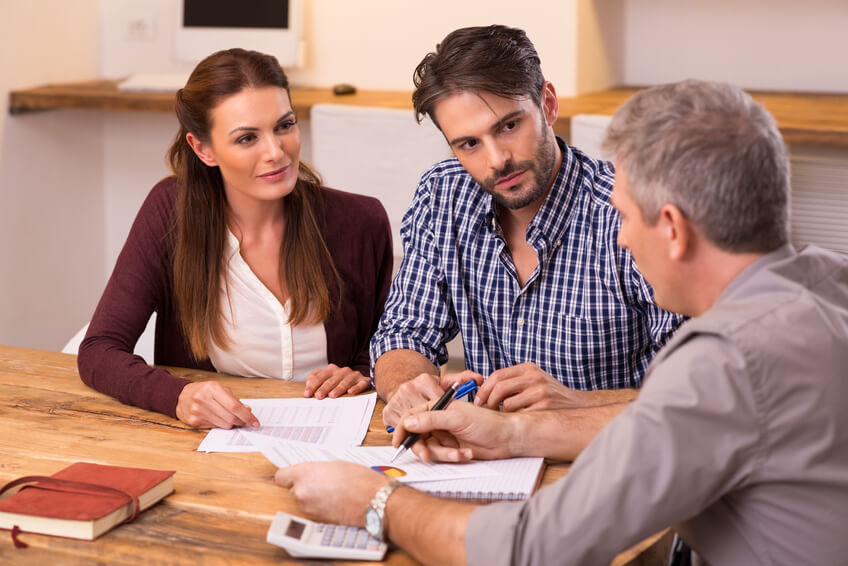 Three people sitting at a table discussing documents, representing a collaborative estate planning or financial consultation.