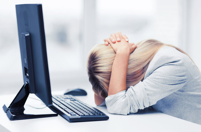 Person sitting at a desk with their head resting on folded arms in front of a computer, representing frustration or overwhelm—ideal for illustrating estate planning challenges.